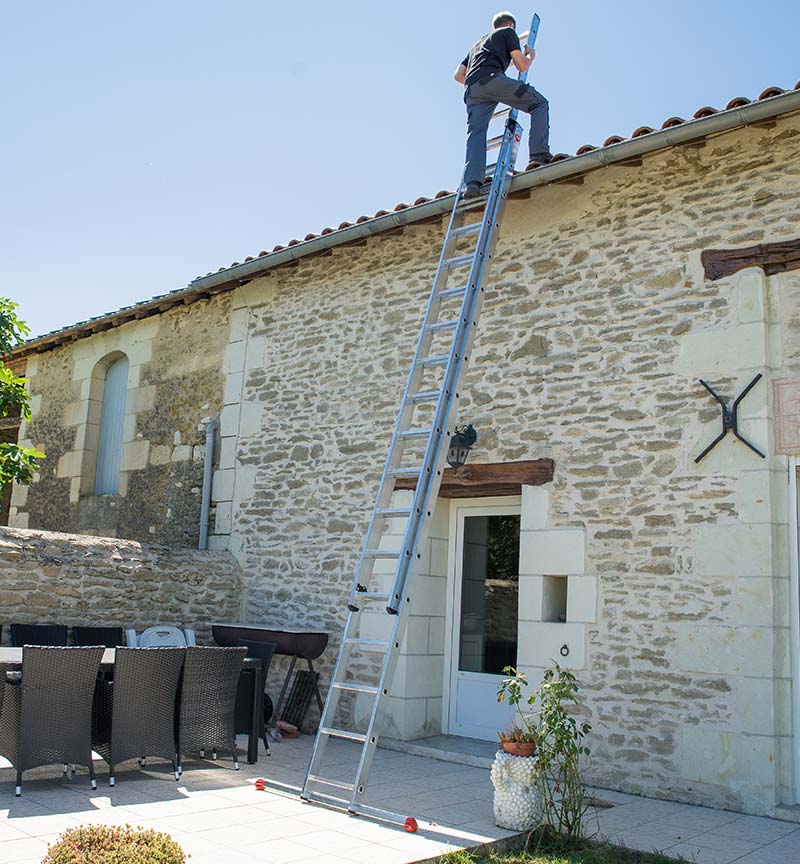 homme montant sur son toit à l'aide d'une échelle